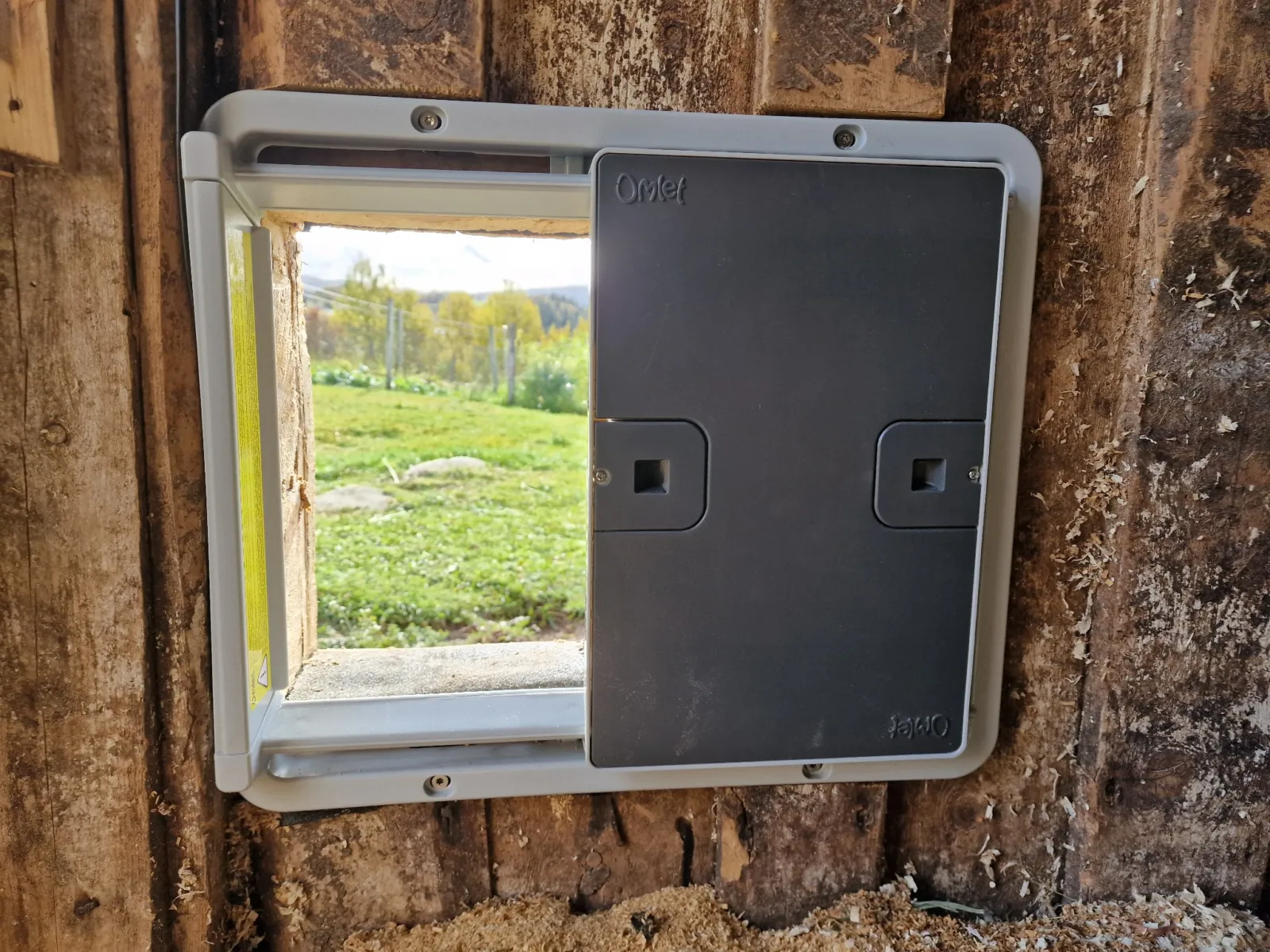 Grå Omlet Smart Autodoor ferdig montert på innsiden av fjøsveggen, med luken halvt åpen.